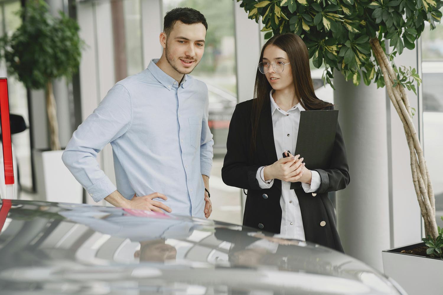 Myyjä ja asiakas autoliikkeessä auton äärellä